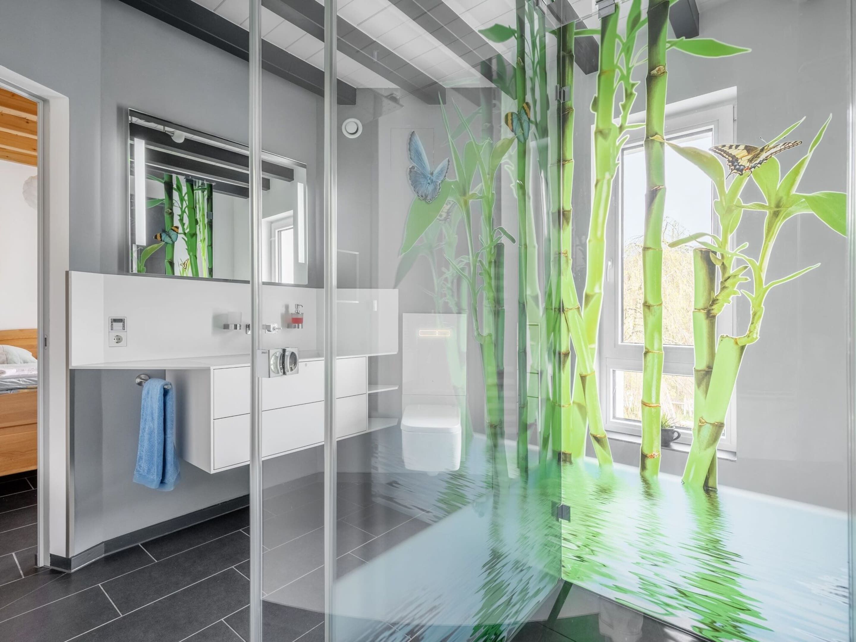 A modern bathroom with a glass partition, a mirror, a sink, and a towel rack.