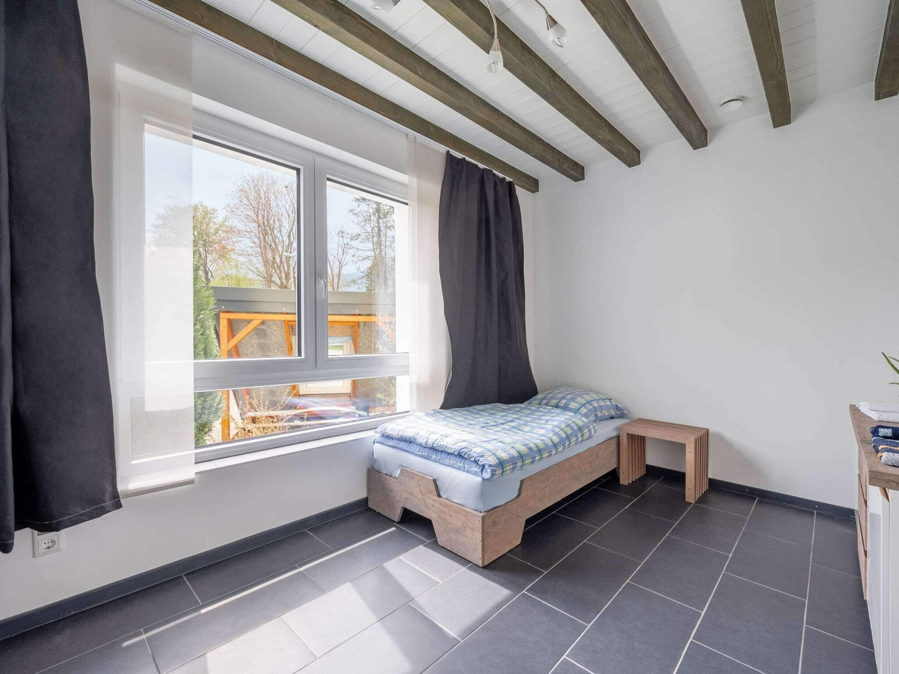 Een slaapkamer met een bed, een raam, een bankje en een bureau.