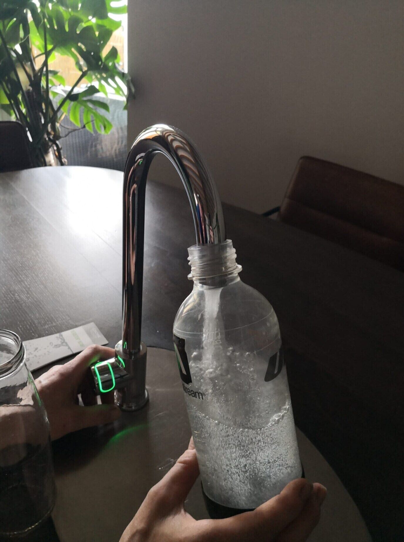 Eine Flasche unter einem Küchenarmatur, in die Wasser fließt.