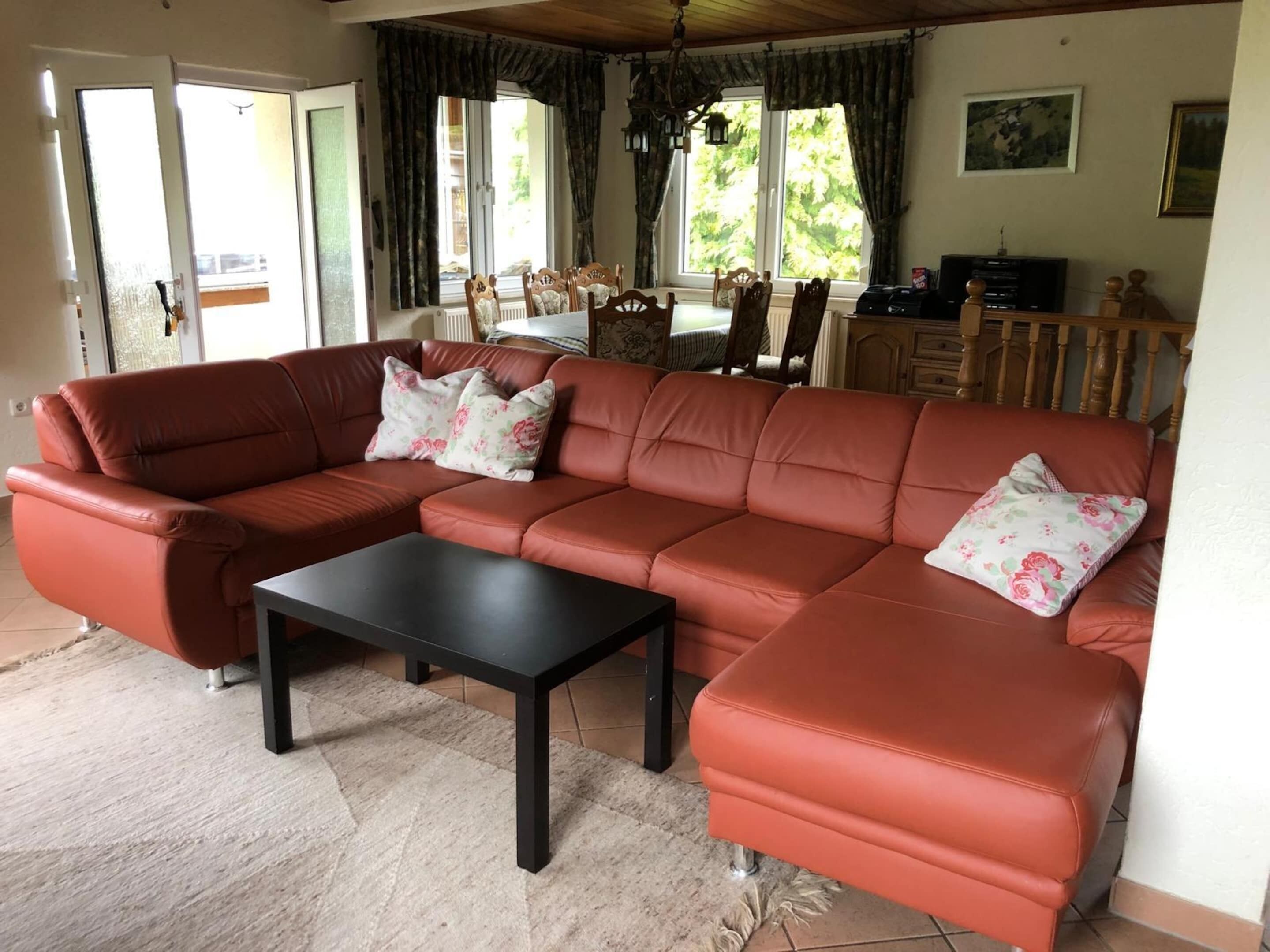A living room with a sectional sofa, a coffee table, and a dining area with chairs and a table.