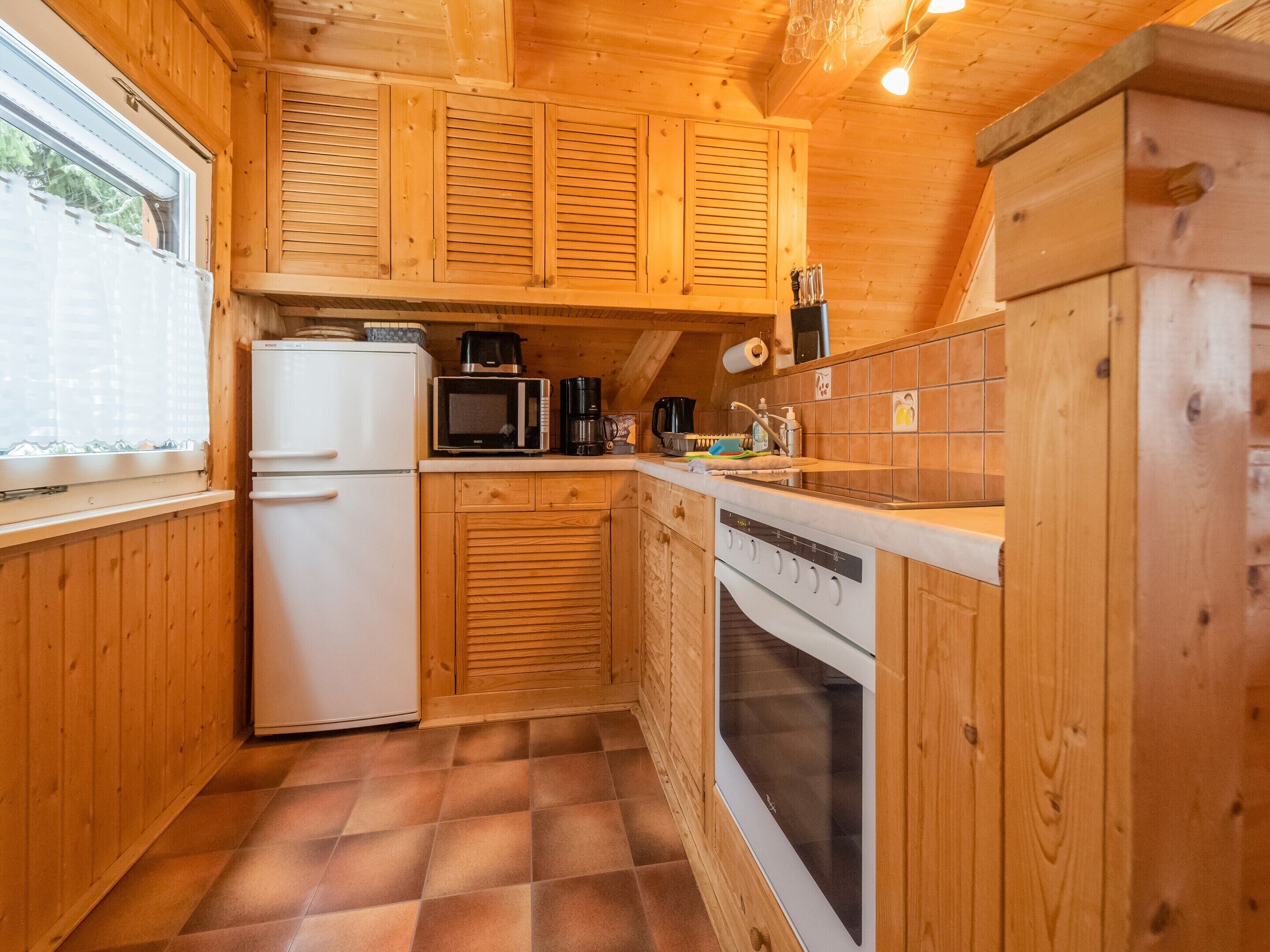 Una cocina compacta con armarios de madera, un refrigerador blanco, un microondas, una cafetera y un lavamanos.