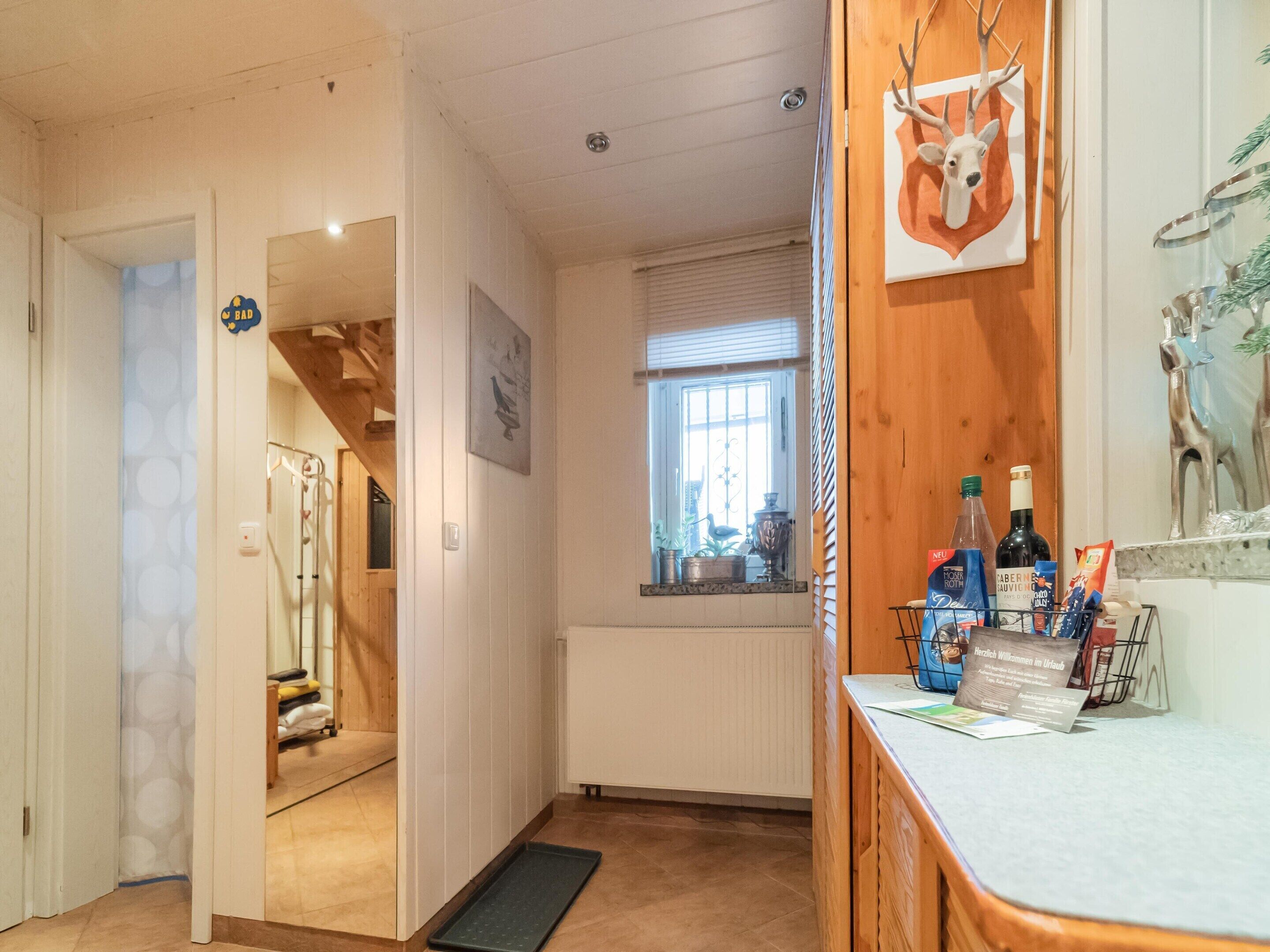 Una habitación de hotel con techo de madera, una ventana con persianas, un radiador, una puerta de madera y una decoración de cabeza de ciervo montada en la pared.