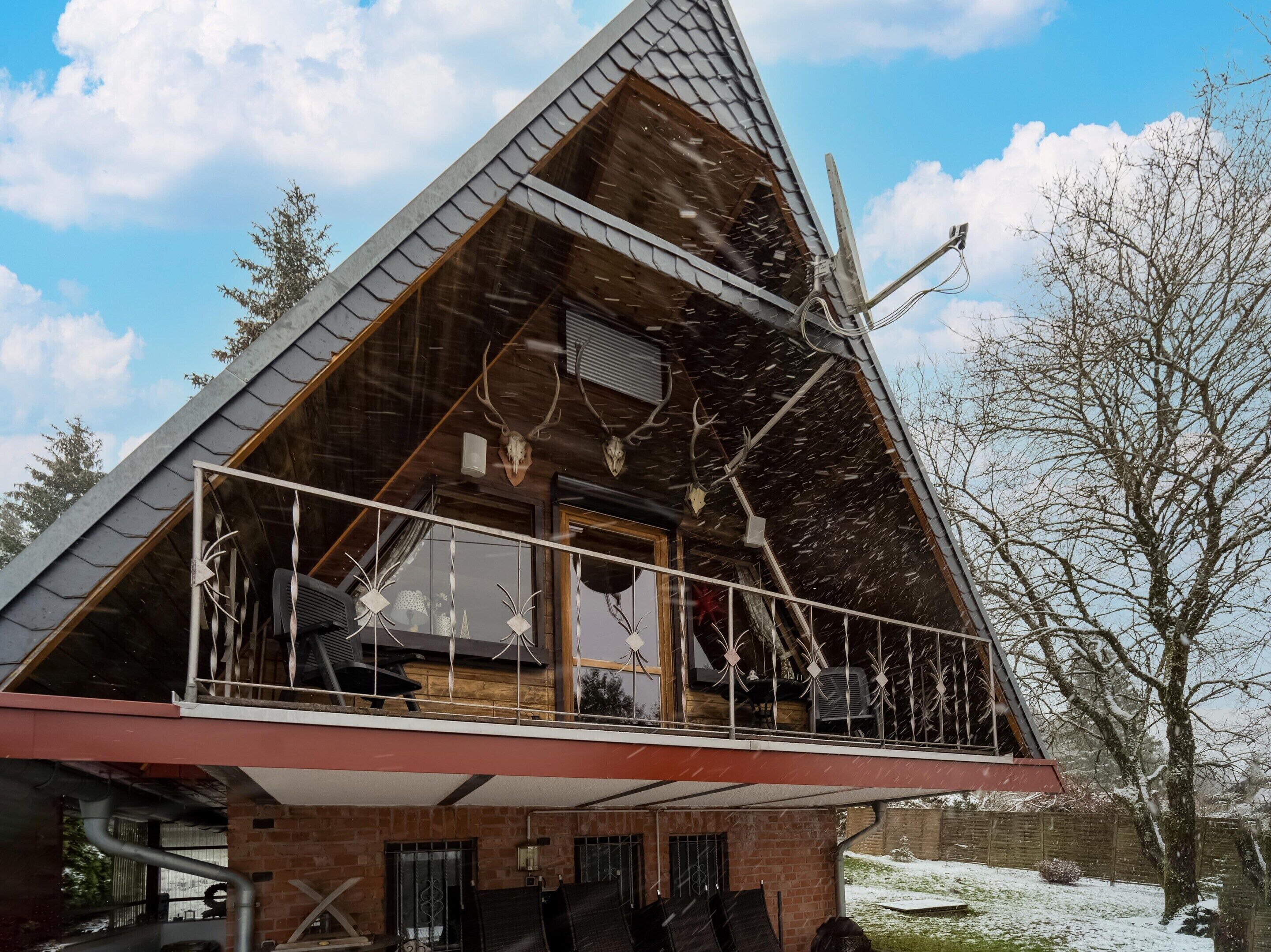 Une maison moderne avec un toit en pente, un balcon doté de rampes en métal et des fondations en briques.