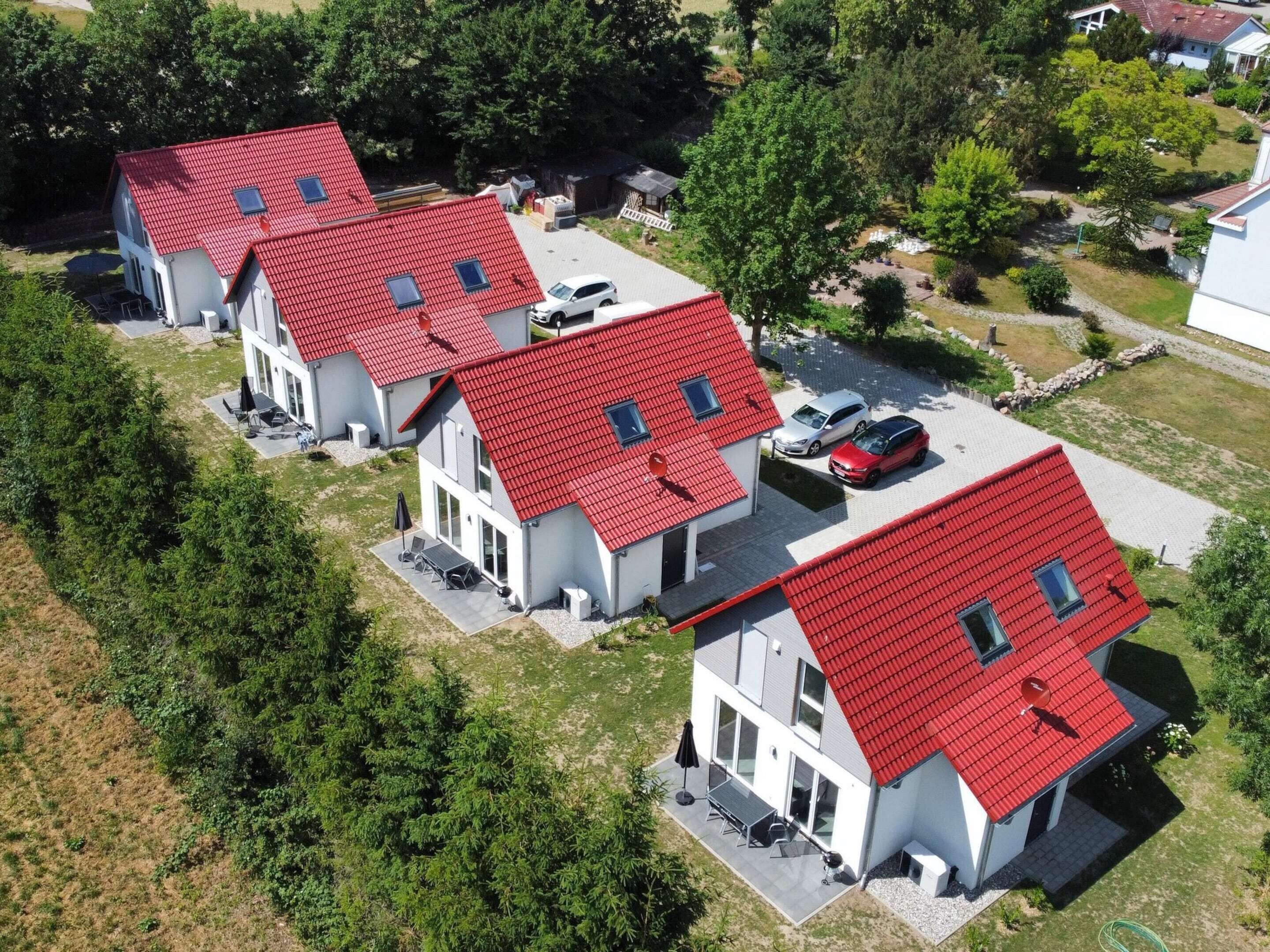 Filas de casas modernas de dos pisos con tejados rojos y ventanas grandes, rodeadas de vegetación y un estacionamiento.