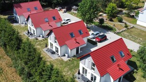 Eine Reihe moderner, zweigeschossiger Häuser mit roten Dächern und großen Fenstern, umgeben von Grünflächen und einem Parkplatz.