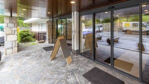 A stone-floored entrance with a wooden ceiling, glass doors, and a view of a parking area with vehicles.