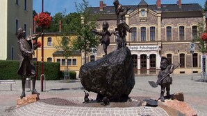 A public square with a central fountain, surrounded by buildings and a street lamp.