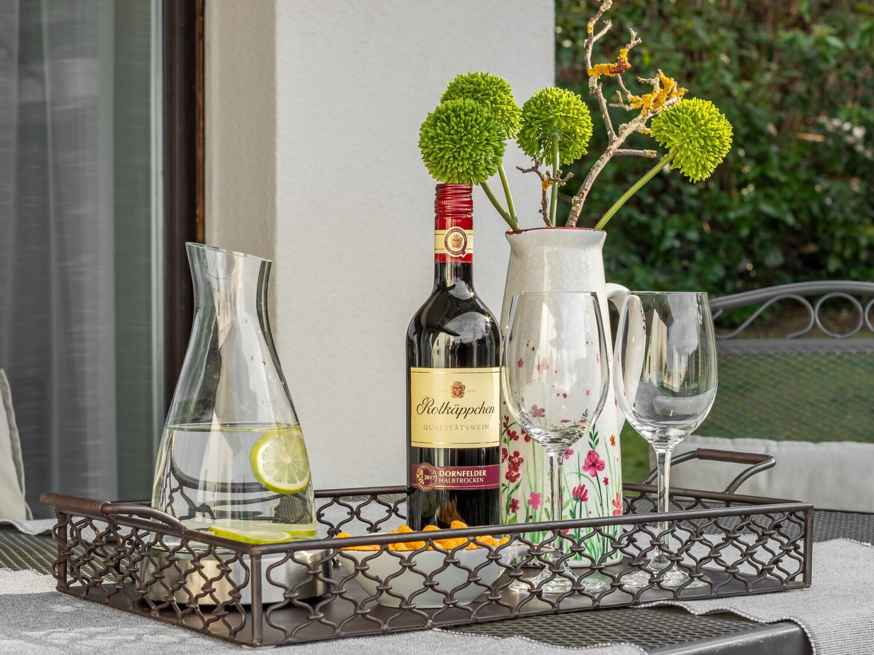 A tray with a wine bottle, a pitcher, and two glasses, accompanied by a vase with flowers and a glass container with citrus slices.
