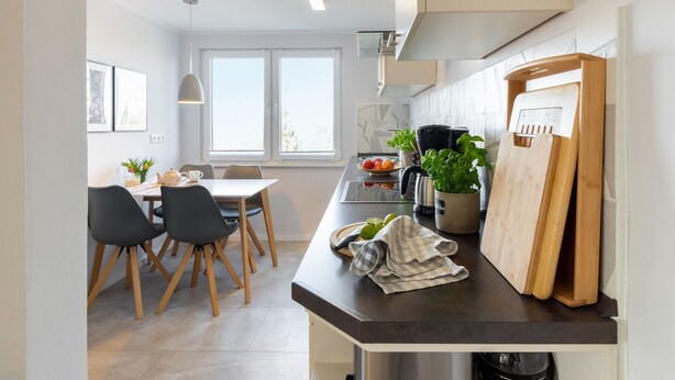 Een moderne keuken met een eethoek, met een groot raam, een koffieapparaat en een snijplank.