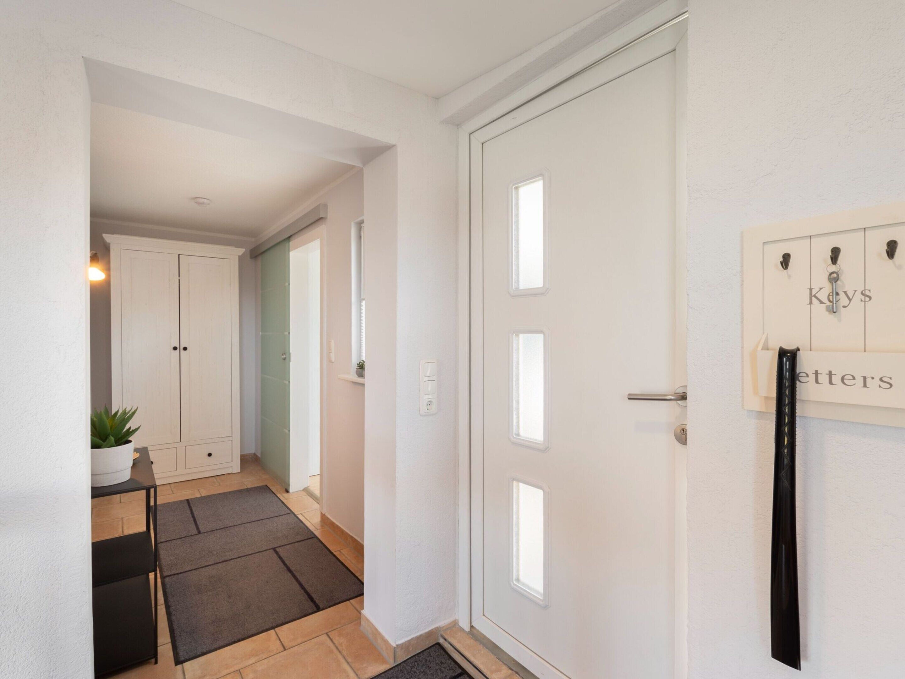 A hallway with a white door, a small table with a plant, and a mat on the floor.