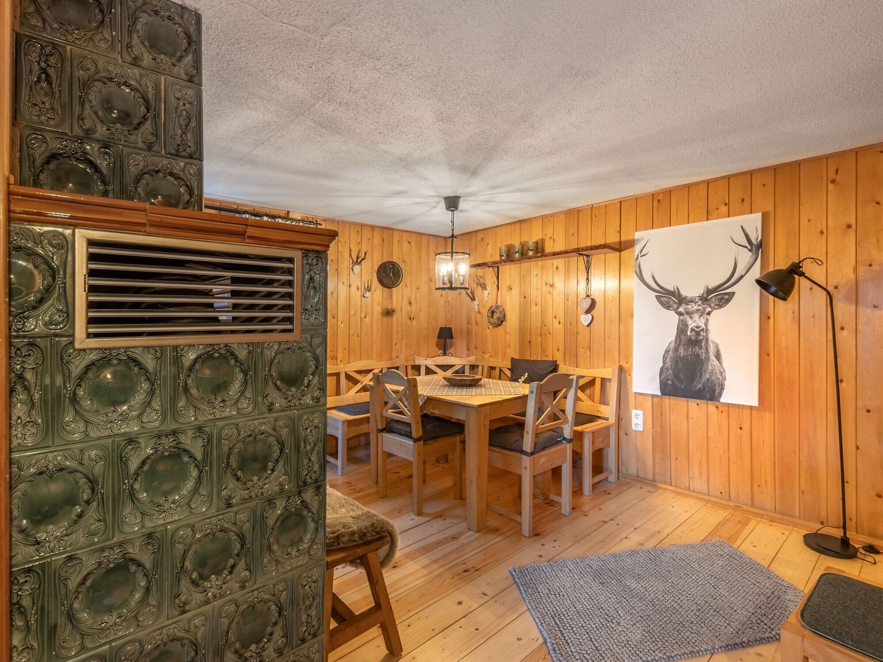 A dining area with wooden walls, a table with chairs, a chandelier, and a deer artwork on the wall.