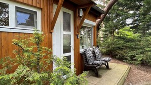 A wooden cabin with a porch, two windows, and a bench with patterned cushions. - Holiday Home With Direct Access to the Beach (Ostseebad Baabe)