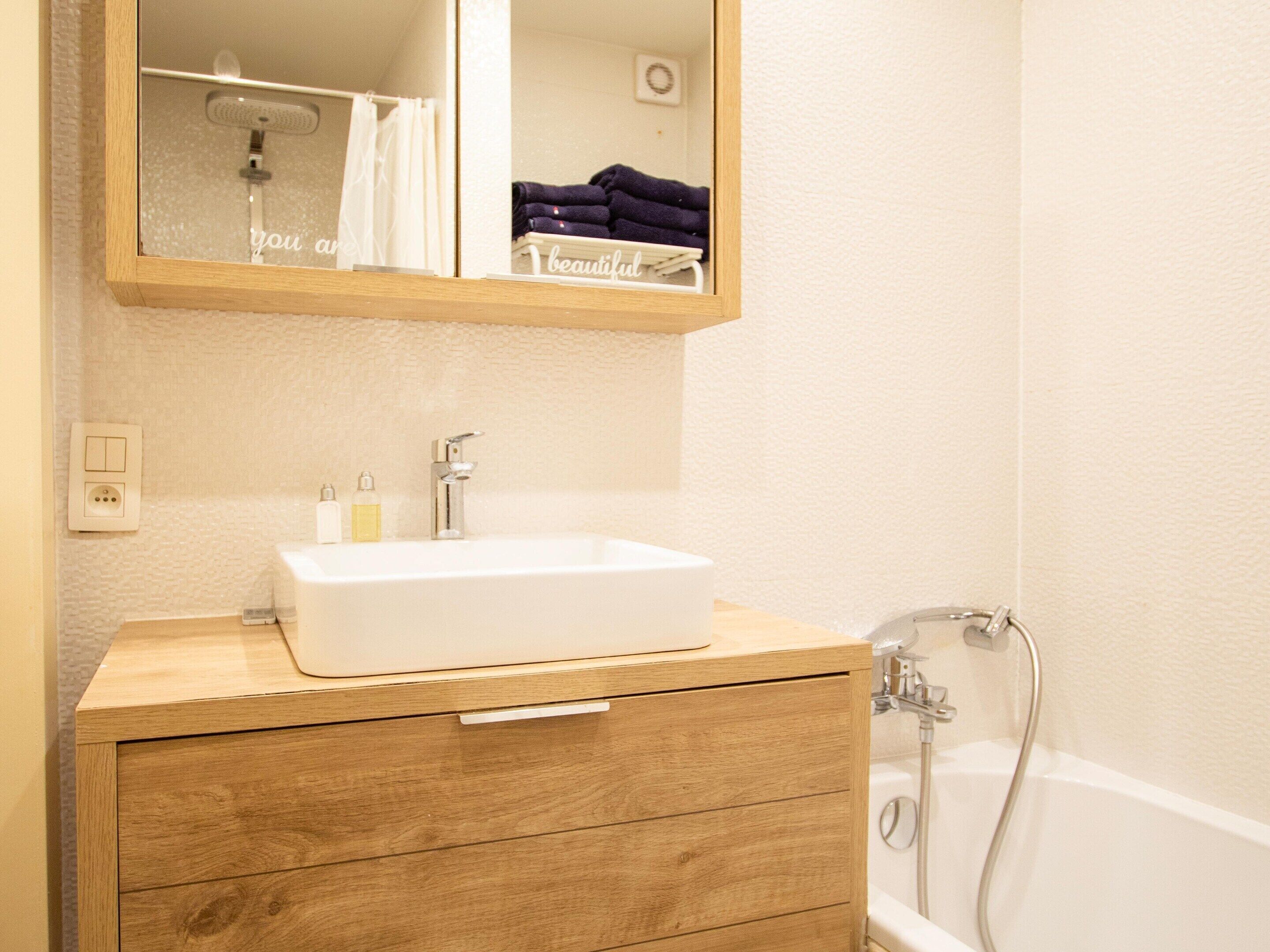 A bathroom with a wooden vanity, a white sink, a mirror, and a shower.
