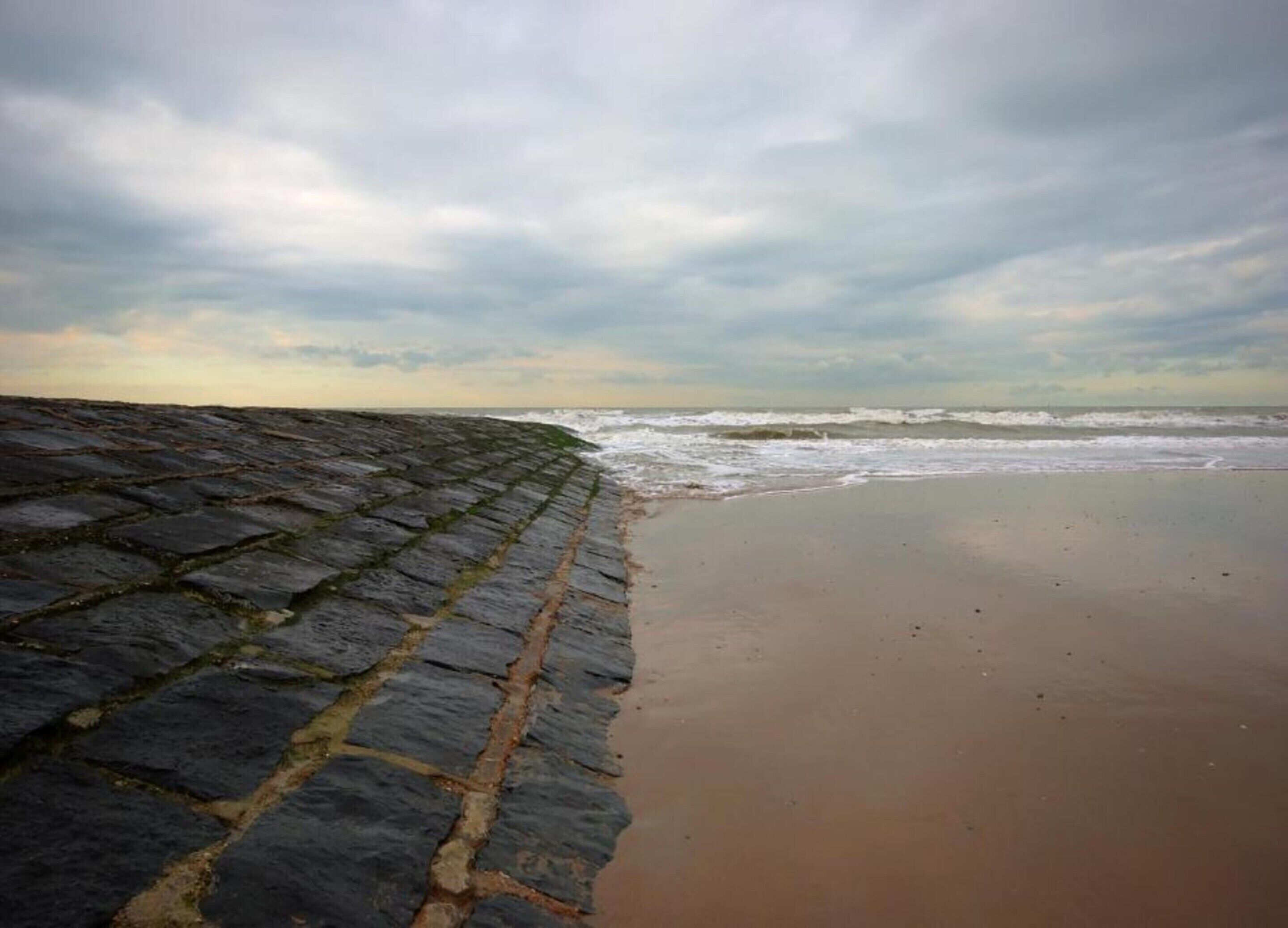 Una playa con un muro de piedra y una orilla arenosa.