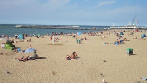 Una playa concurrida, gente tomando el sol y caminando.
