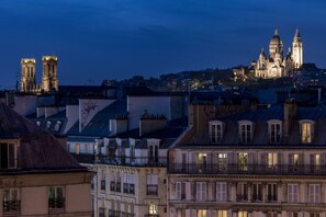 Une vue d’une ville au crépuscule, avec des bâtiments illuminés, dont une imposante cathédrale à deux tours.