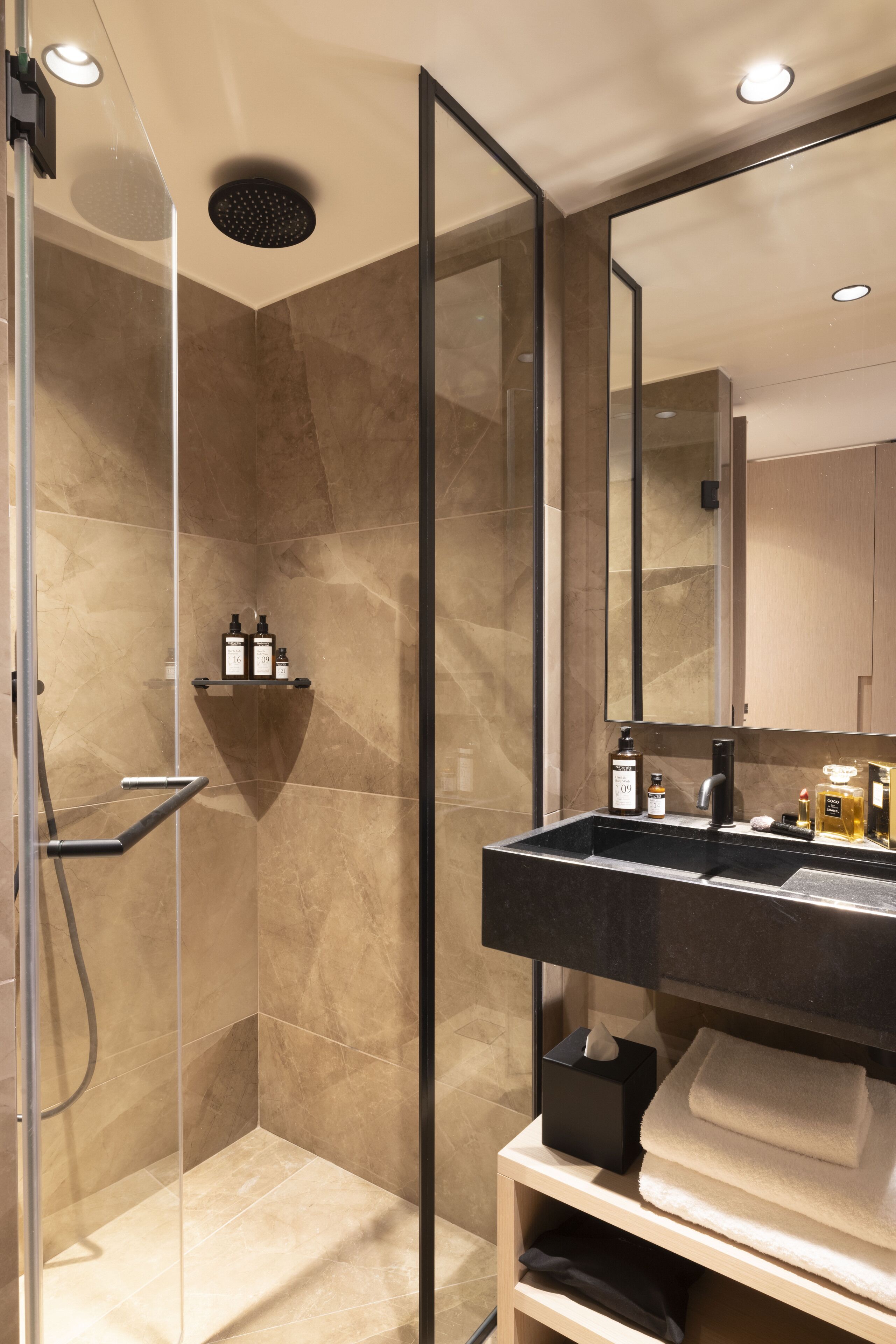 A modern bathroom with a glass-enclosed shower, a large mirror, and a vanity with toiletries.