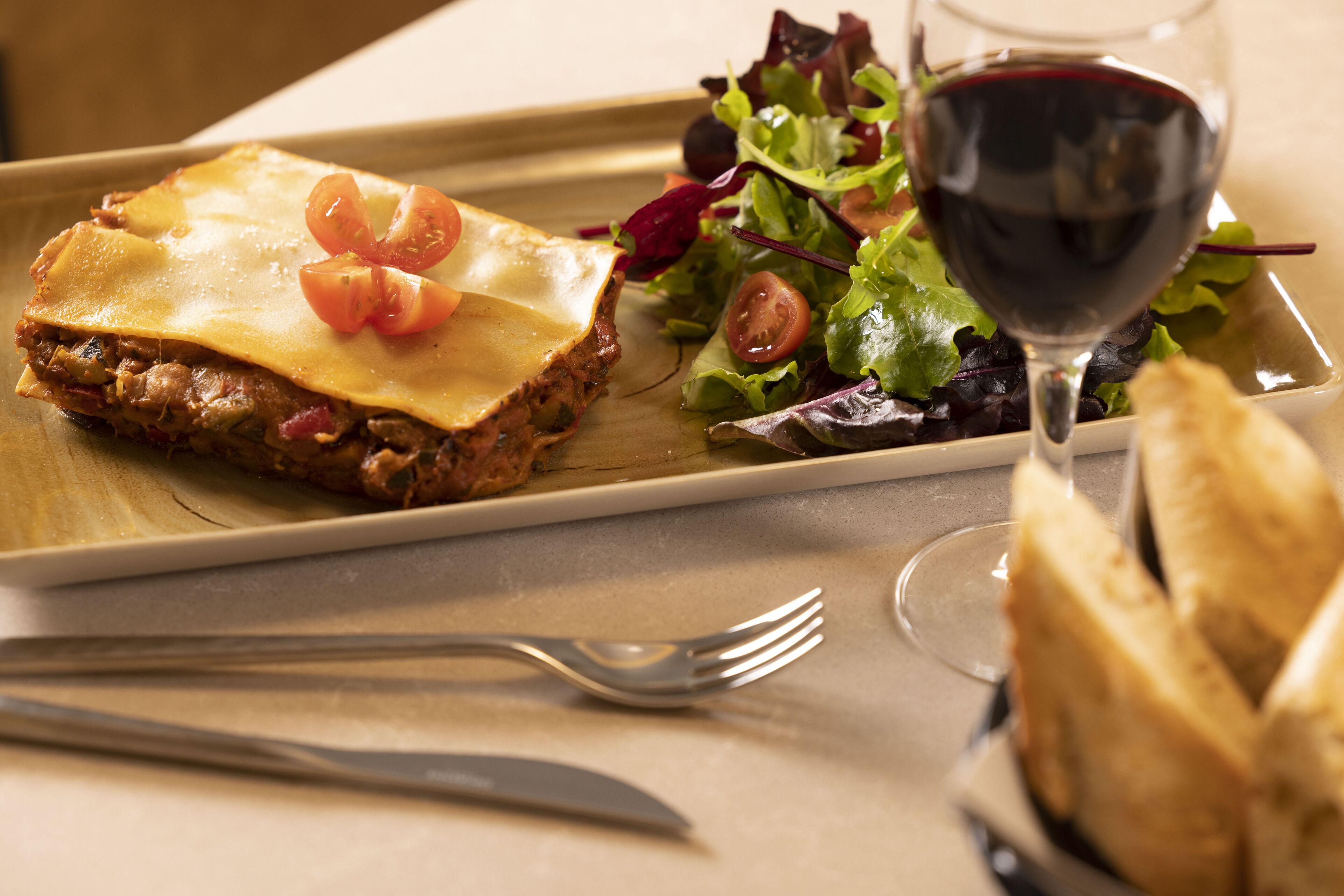 Une assiette avec un plat composé de plusieurs couches, un verre de vin rouge et une salade en accompagnement.