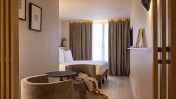 Een hotelkamer met een bed, twee fauteuils, een tafeltje, een nachtkastje met lamp en een raam met gordijnen.