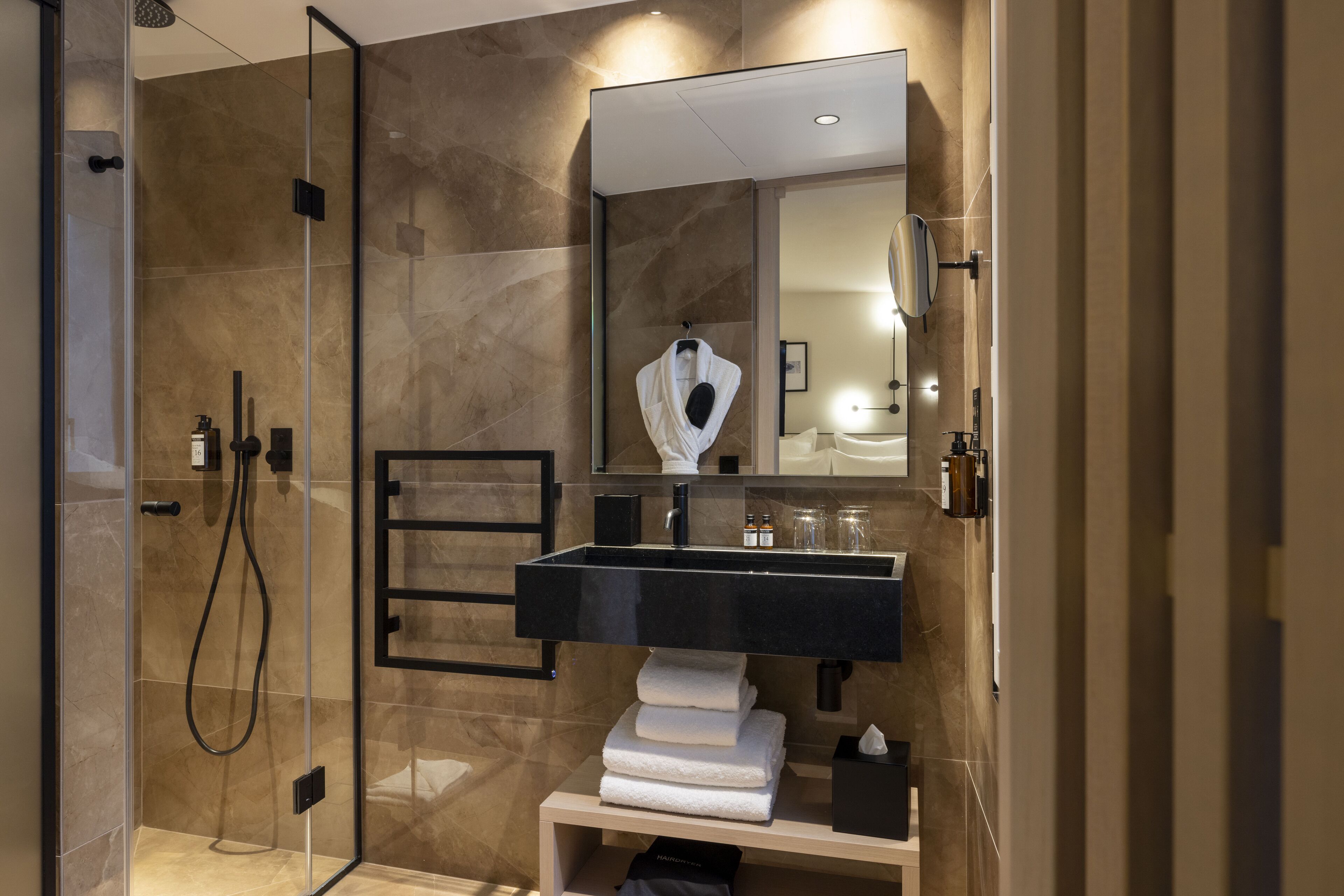 A modern bathroom with a glass-enclosed shower, a black sink, and a mirror above it.