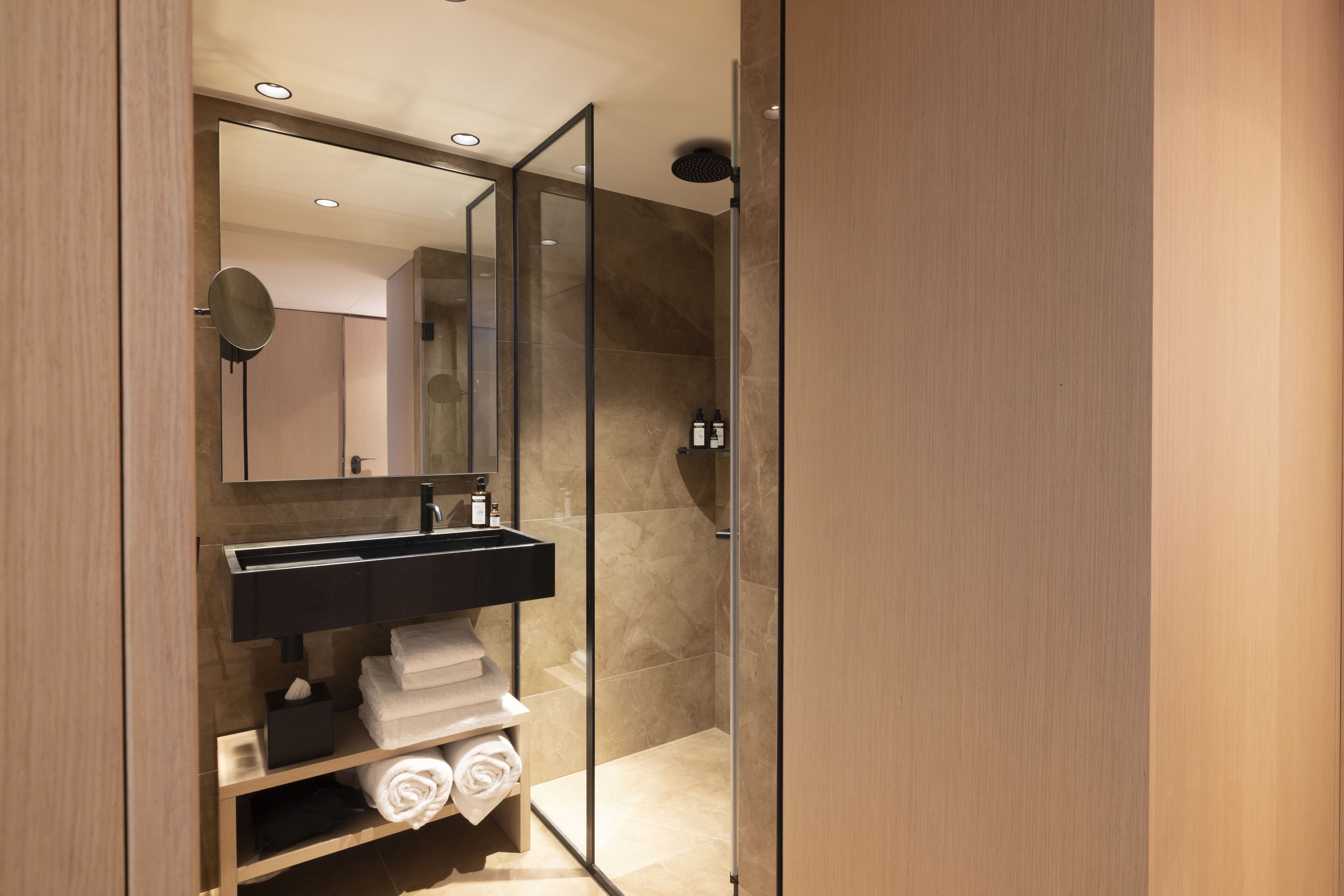 Un baño moderno con cabina de ducha de vidrio, tocador negro y un espejo grande.