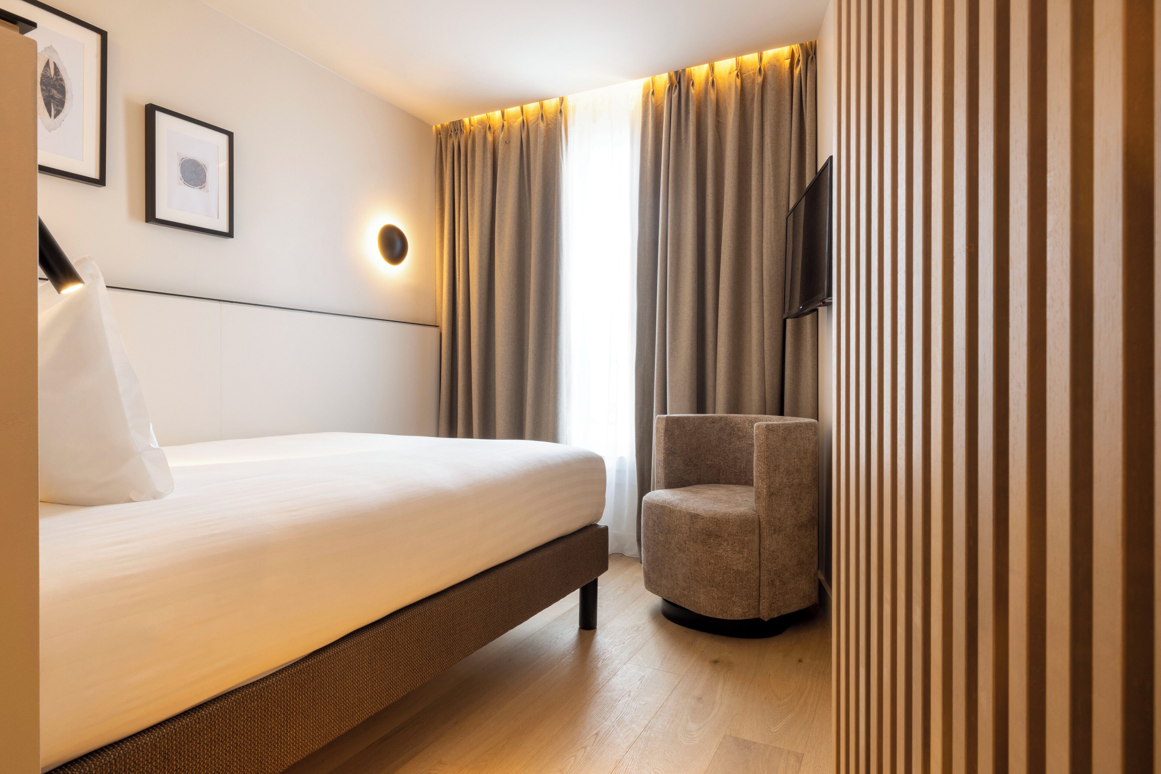 Habitación de hotel moderna con cama, una silla, un televisor de pantalla plana y una lámpara de pared.