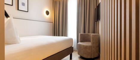 Habitación de hotel moderna con cama, una silla, un televisor de pantalla plana y una lámpara de pared.