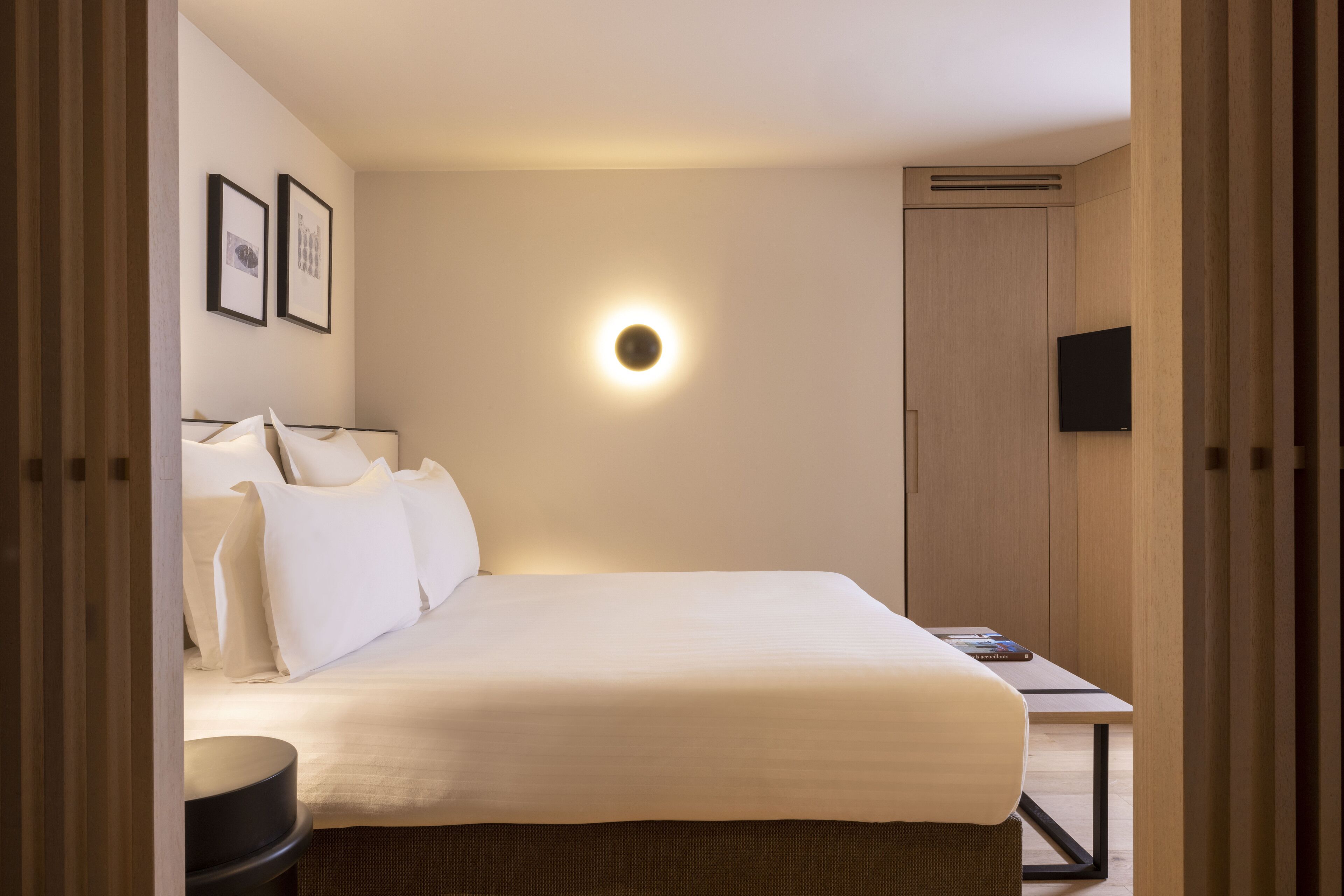 A hotel room with a bed, bedside table, wall-mounted TV, and framed pictures.