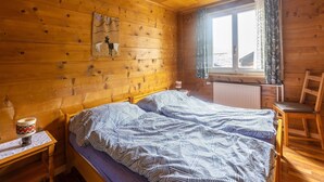 Une pièce de style cabane en bois, comprenant un lit, une chaise, une table, un élément décoratif mural suspendu et une fenêtre avec des rideaux.