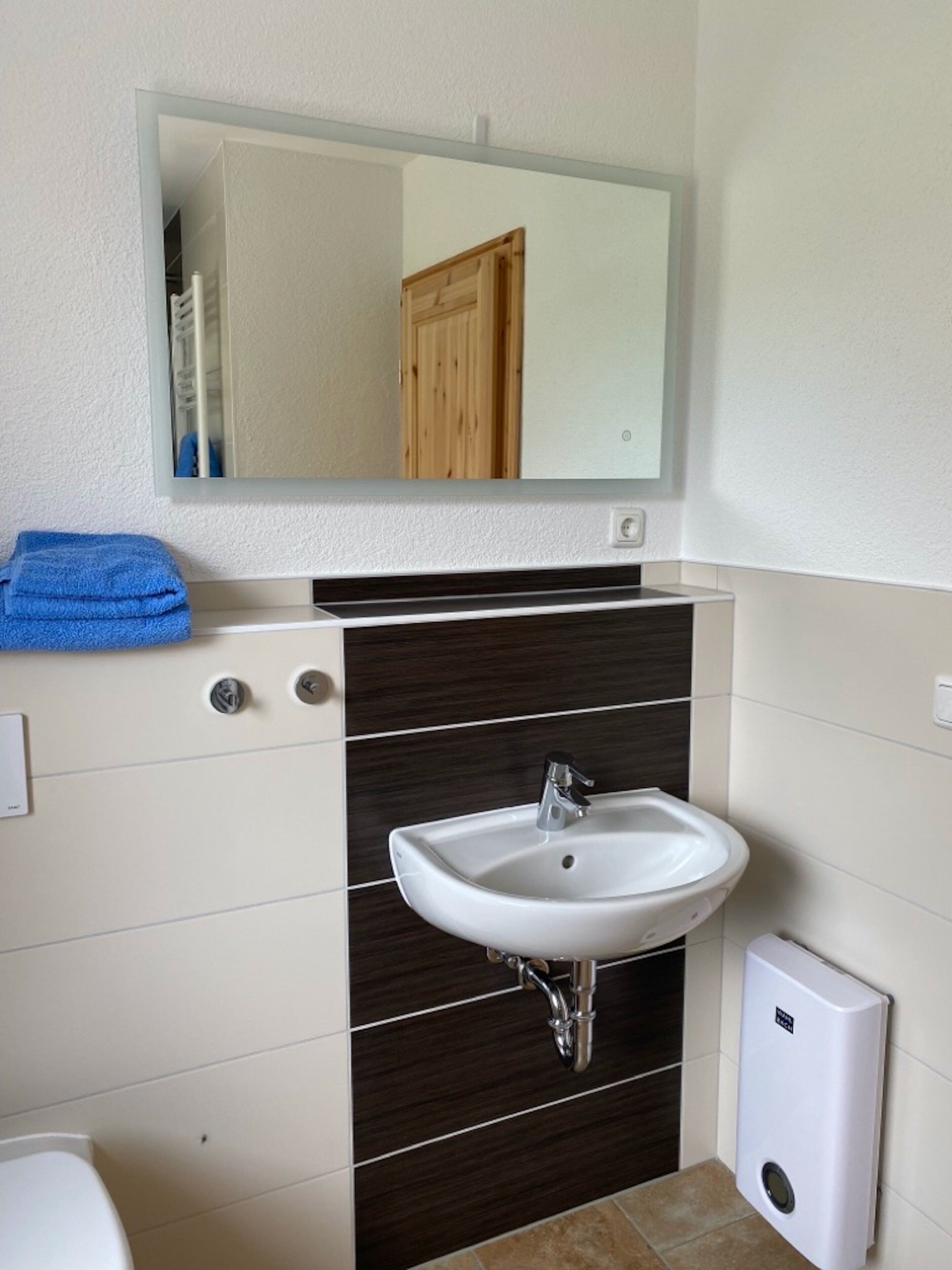 A bathroom with a white sink, a mirror above it, and a towel on the wall.