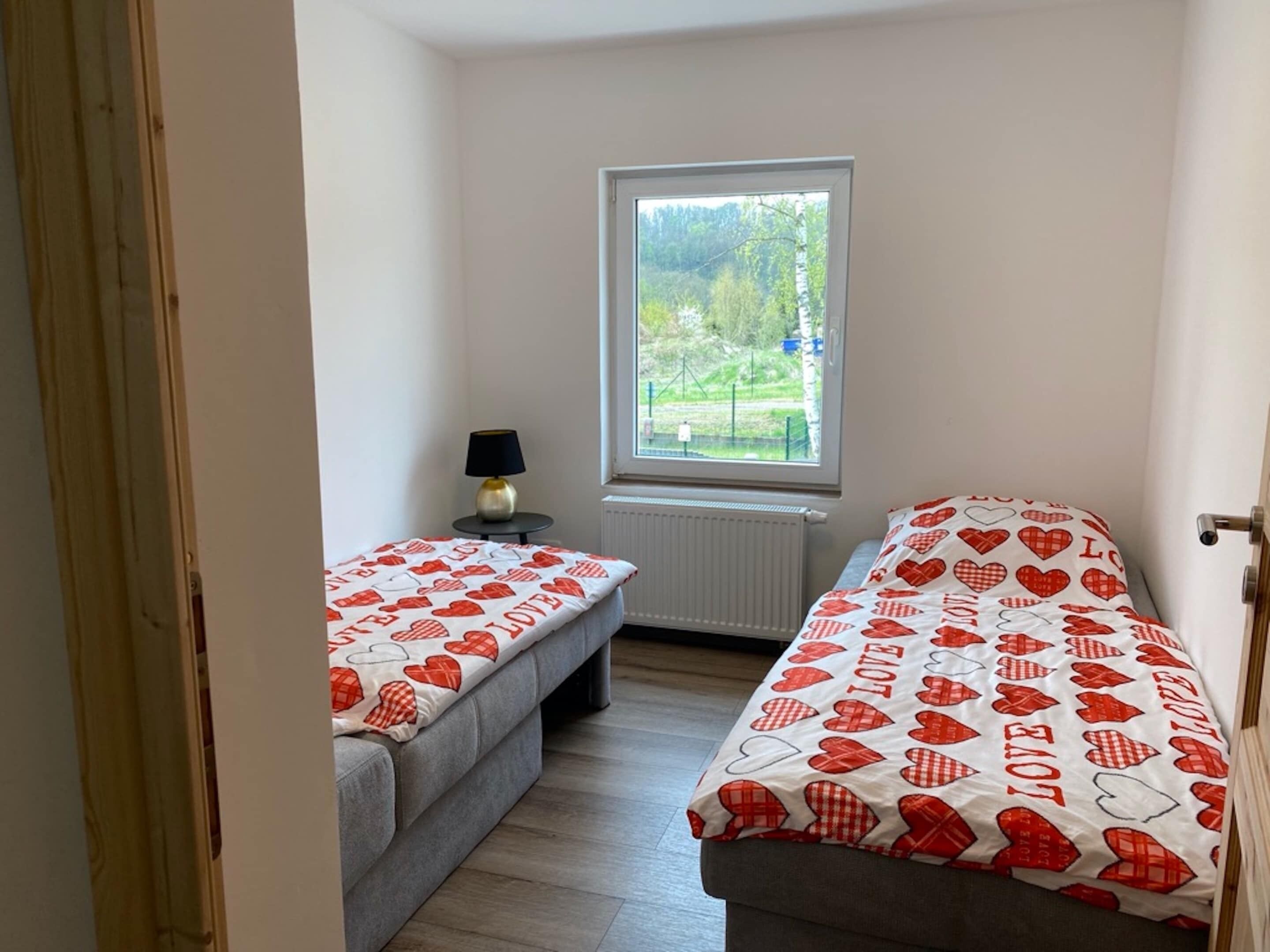 Et lille værelse med to senge, et vindue, en radiator og en lampe.