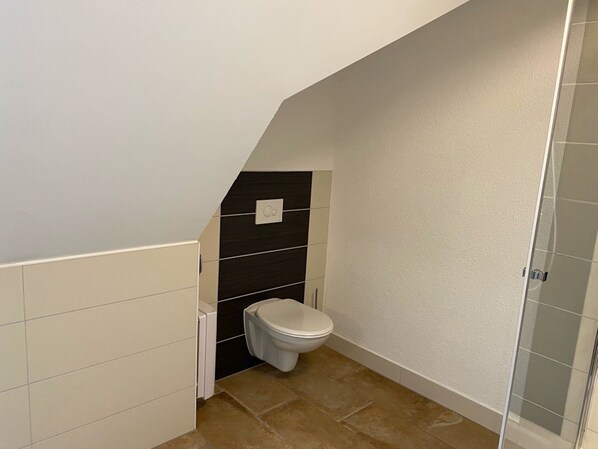 Un baño con inodoro, ducha y piso de baldosas.