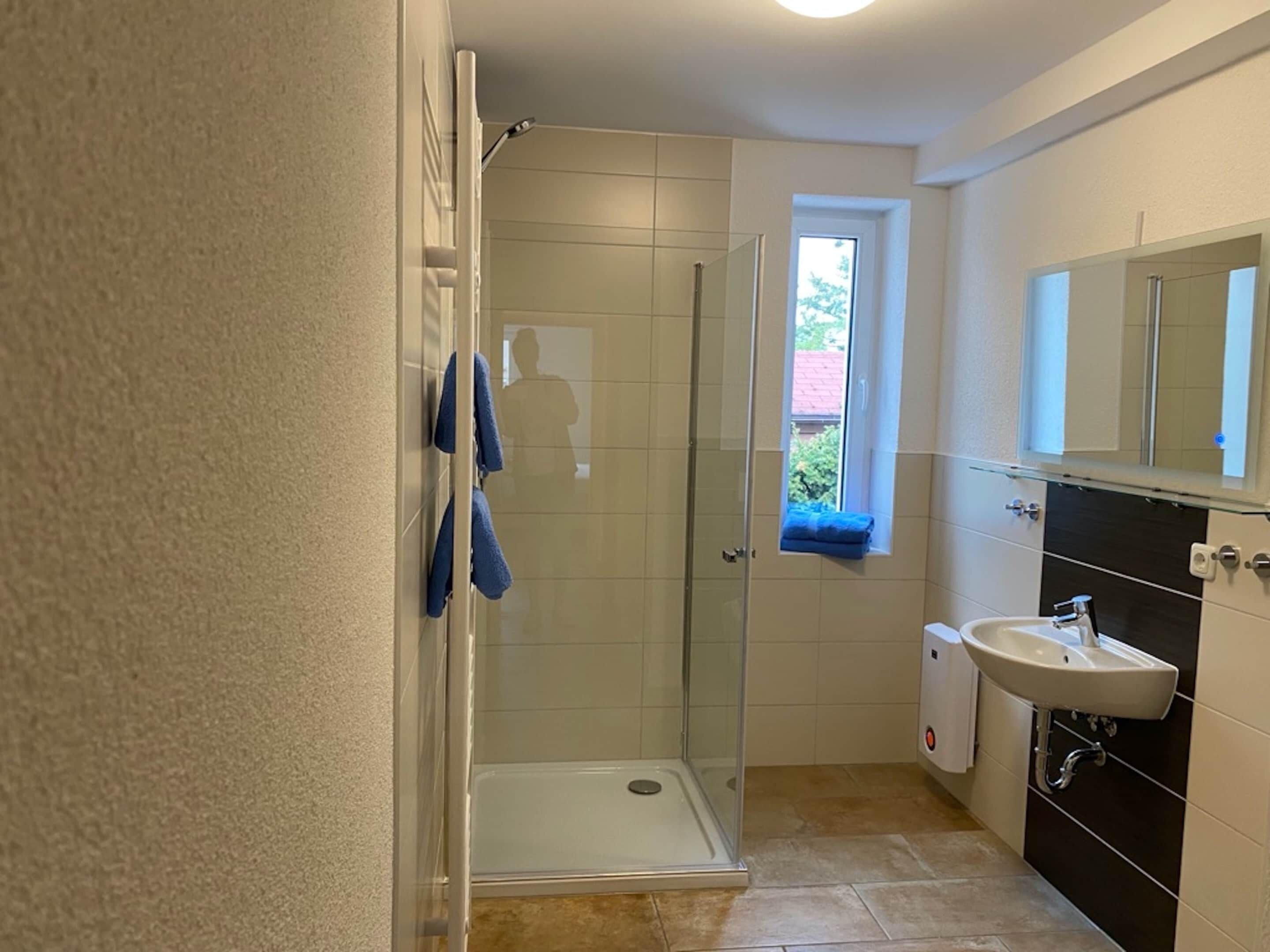 A bathroom with a shower, a sink, and a window.