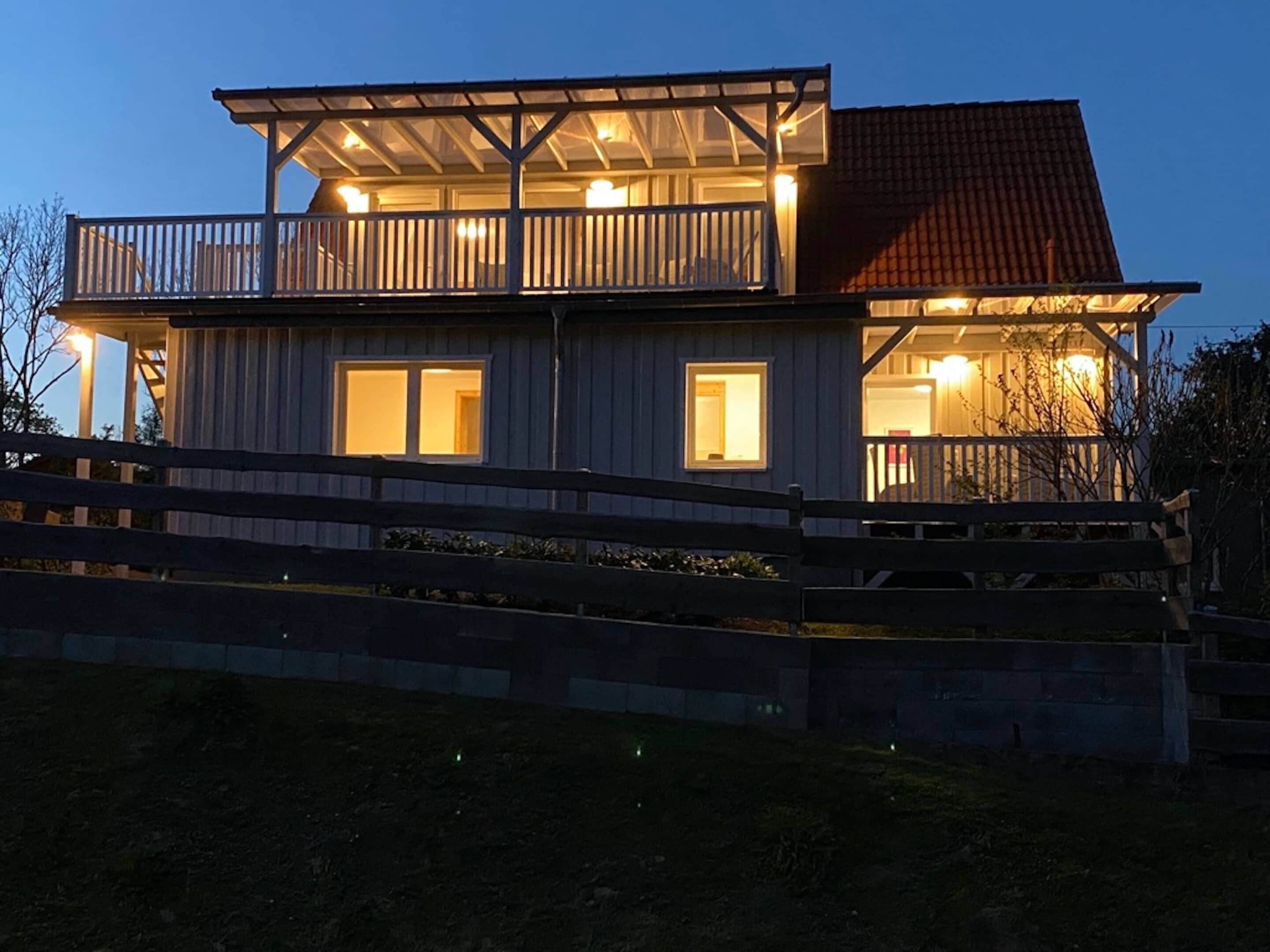 Ein zweigeschossiges Haus mit Balkon, einer Holzterrasse und einem roten Ziegeldach.
