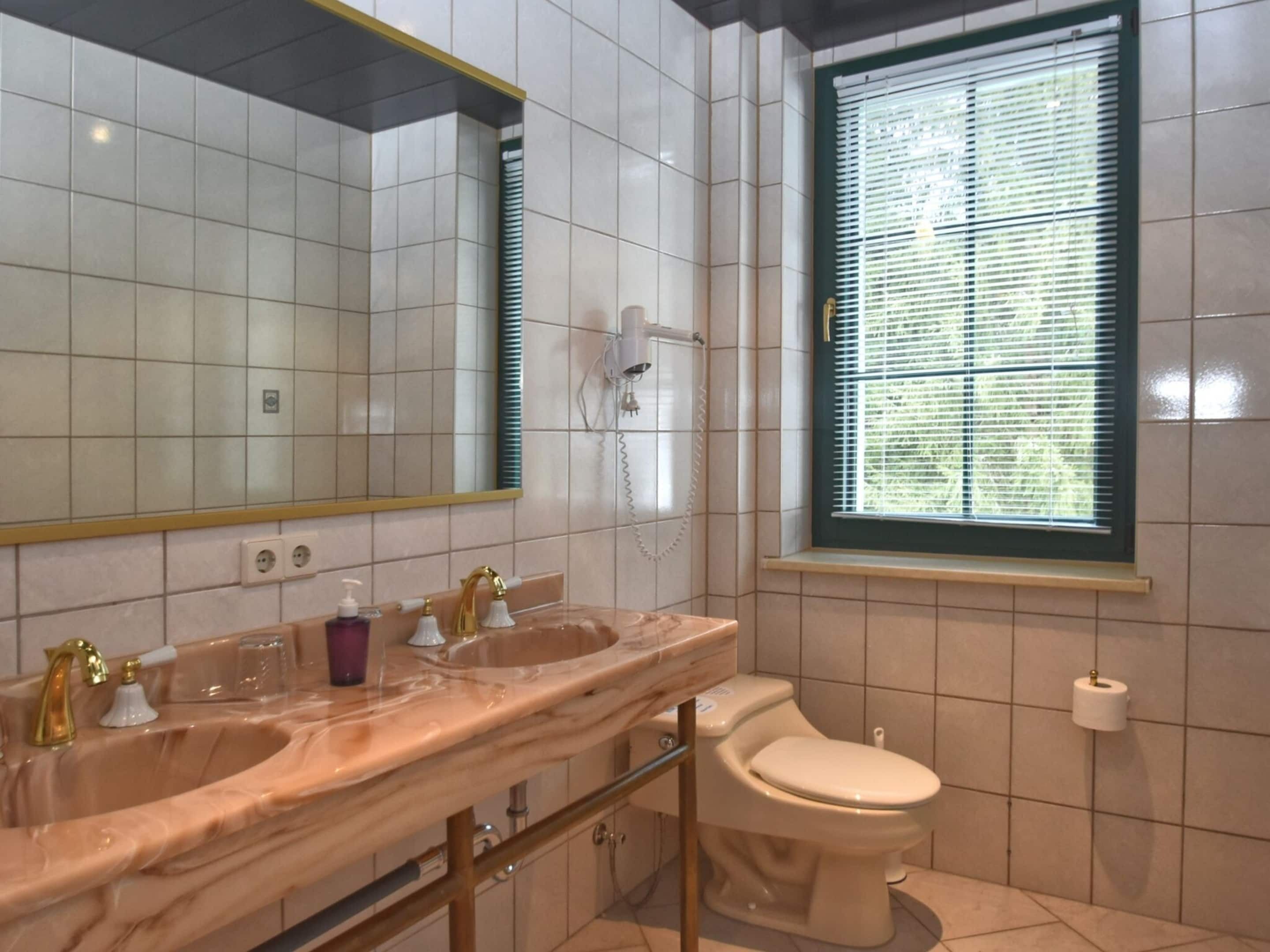 Et badeværelse med vask i marmor, toilet og et vindue med persienner.