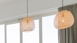 Une pièce dotée de deux luminaires suspendus en fibres tressées et offrant une vue sur l’extérieur grâce à de grandes fenêtres.