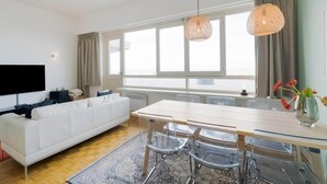 Un salon moderne avec un canapé blanc, une table à manger en verre et une grande fenêtre.