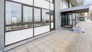 Un bâtiment moderne doté de grandes fenêtres, d’une entrée abritée et d’un trottoir dallé.