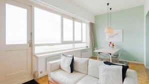 Un salon moderne avec un canapé blanc, une table à manger avec des chaises, un radiateur et une fenêtre avec des rideaux.
