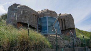 Een betonnen bunker met een glazen uitkijkschot, omringd door hekken en gras.