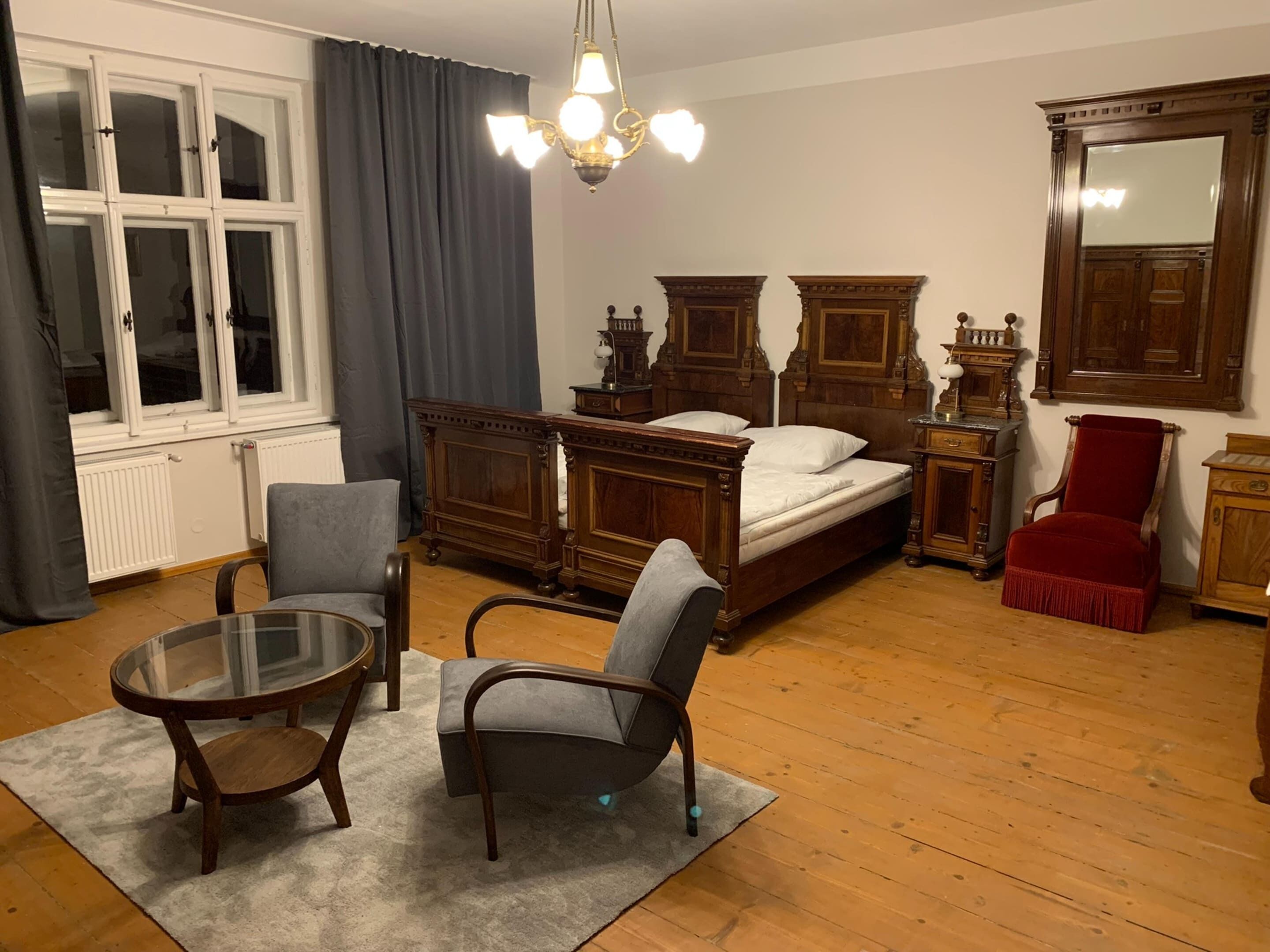 Ein Schlafzimmer mit einem hölzernen Bett, zwei Stühlen, einem Glastisch, einem roten Sessel und einer Kandelaber.