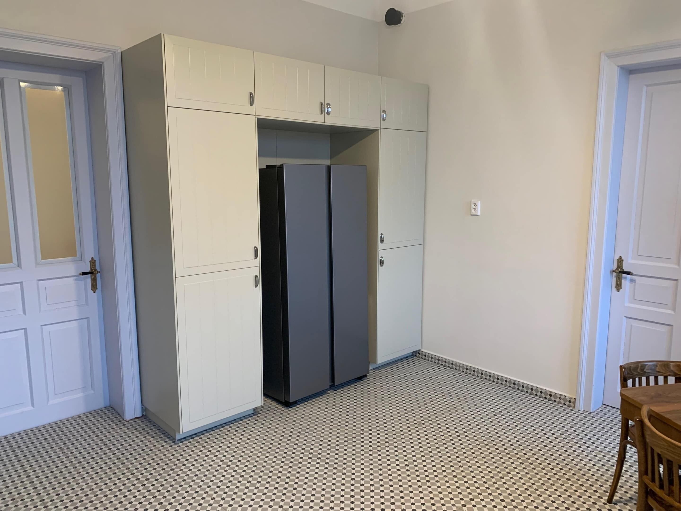 A room with a white tiled floor, a white wardrobe with multiple doors, and a black refrigerator.