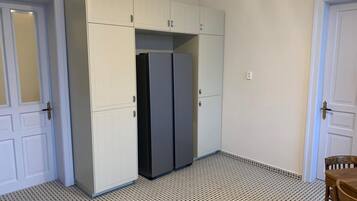 A room with a white tiled floor, a white wardrobe with multiple doors, and a black refrigerator.