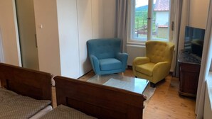 A bedroom with a bed, a wardrobe, a blue armchair, a yellow armchair, a glass coffee table, and a TV on a wooden cabinet. - Spacious Holiday Home in Sluknov With Private Garden (Sluknov)