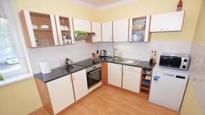 Uma cozinha compacta com armários brancos, bancada preta, forno embutido, pia, micro-ondas e máquina de lavar louça.