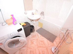 A bathroom with a washing machine, a sink, a bathtub, and a shower.