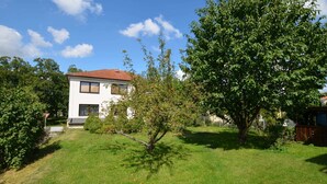 A two-story house with a red-tiled roof, surrounded by a well-maintained lawn and several trees. - Cozy Apartment in Eastern Bohemia Near Town Center (Vysoke Myto)