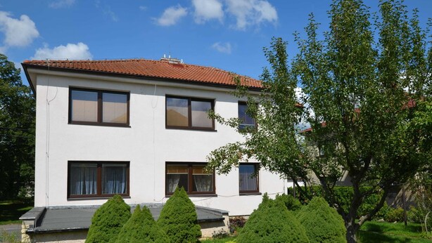 A two-story building with a red-tiled roof, multiple windows, and a well-maintained garden with various shrubs and a large tree. - Cozy Apartment in Eastern Bohemia Near Town Center (Vysoke Myto)
