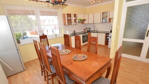 A dining area with a wooden table and chairs, a kitchen in the background, and a view of the outside through a window. - Cozy Apartment in Eastern Bohemia Near Town Center (Vysoke Myto)