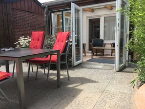 Eine Terrasse im Freien mit Tisch und Stühlen, einer Ziegelwand und einer Glasschiebetür, die zu einem Innenbereich führt.